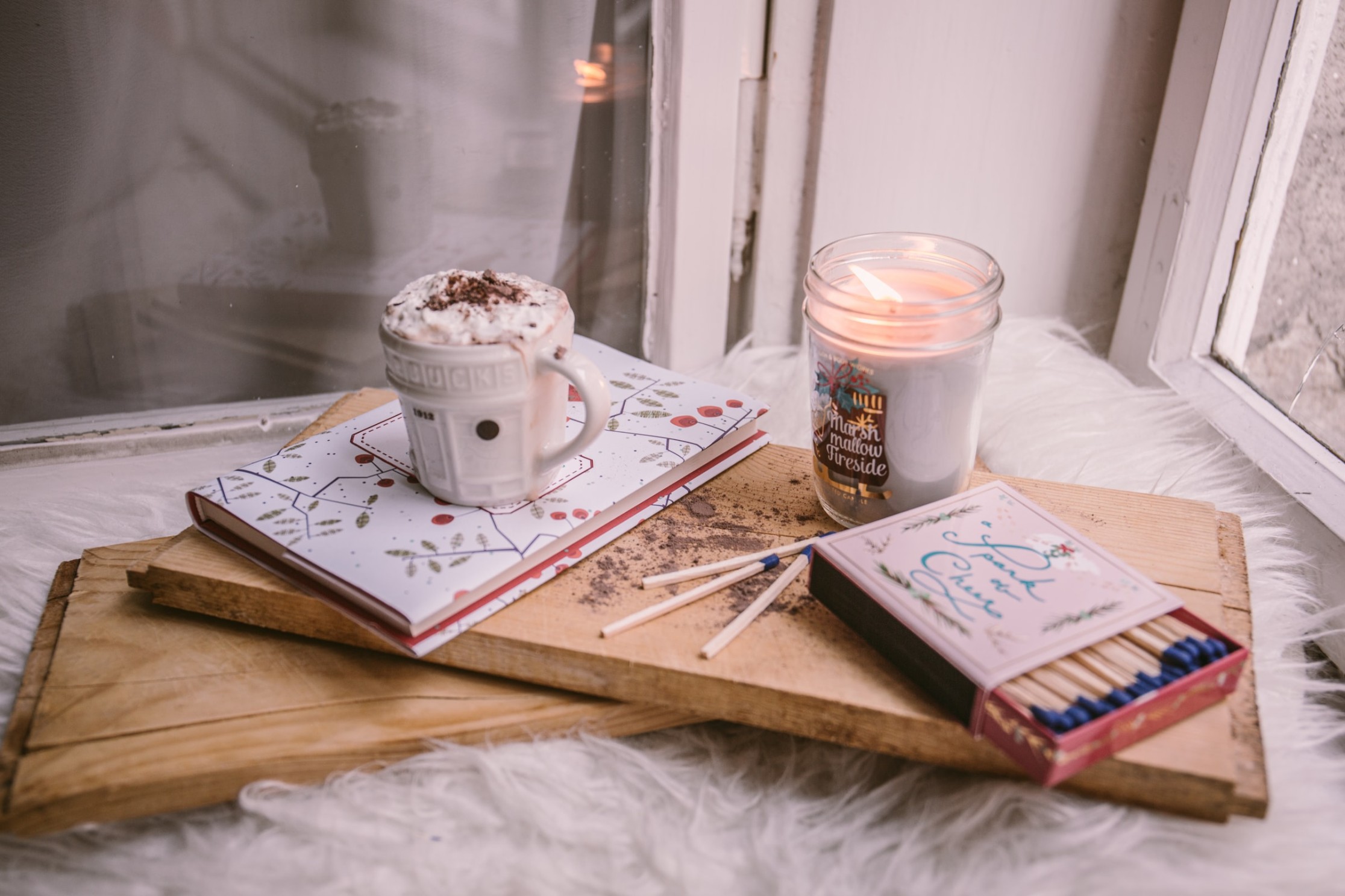 A cosy collection of soothing items — soft fabrics, candle, hot drink and small comforts