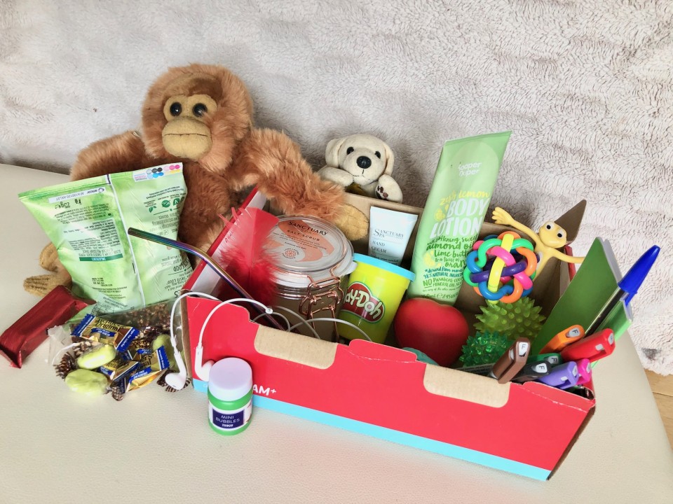 An open shoe box containing soothing items — small toys, photos, scented items and notes