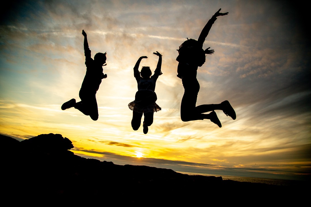 Three silhouettes jumping joyfully against a golden sunset sky